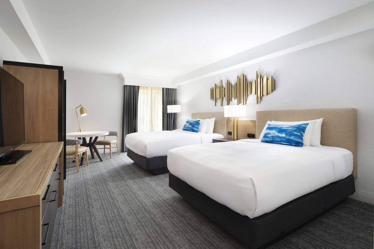 A hotel room with two beds, a desk, and a dining area.
