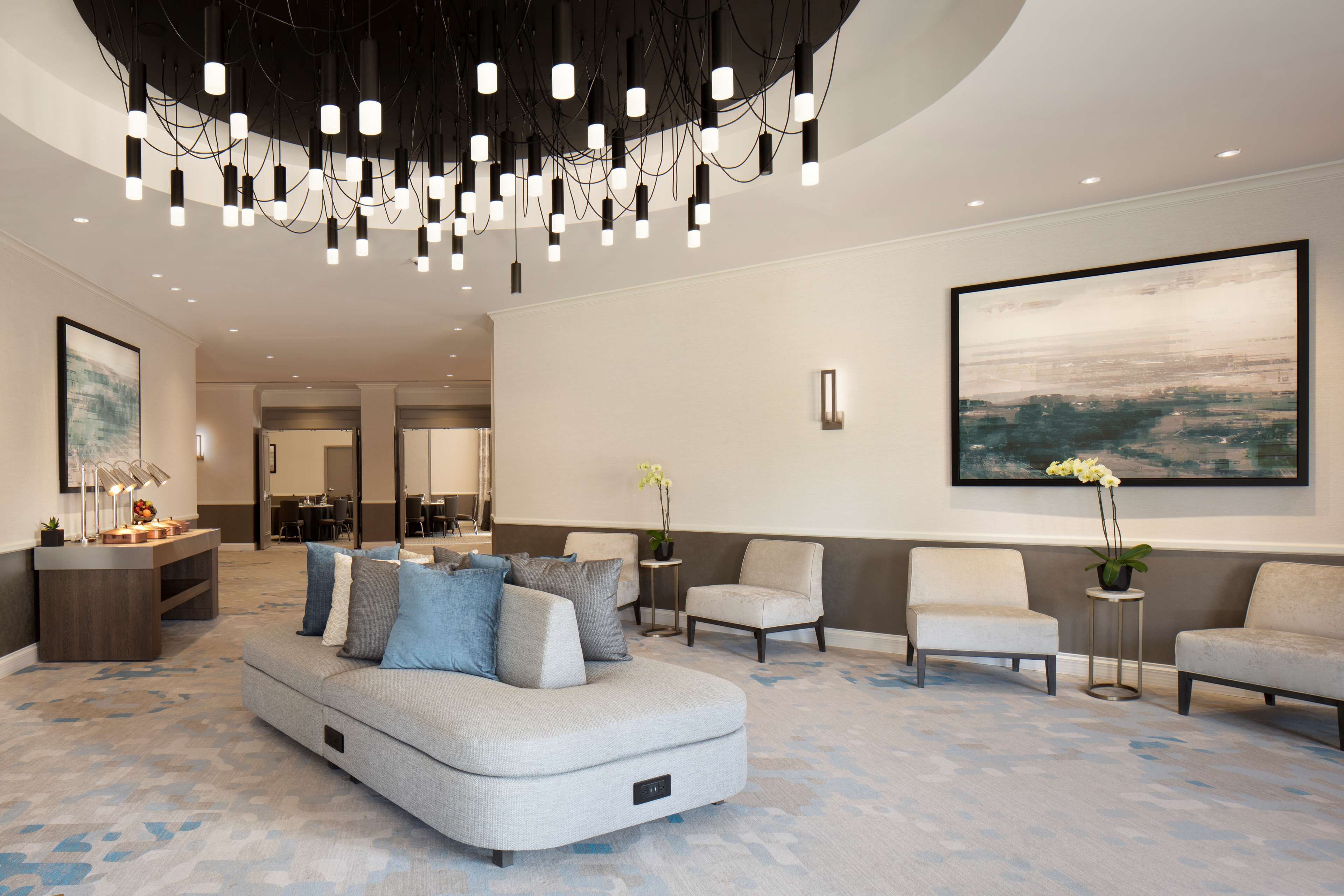 A spacious lobby with a modern sofa, two armchairs, a small table with a plant, and a large abstract painting on the wall.