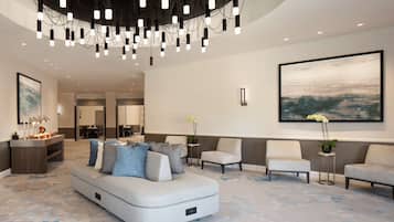 A spacious lobby with a modern sofa, two armchairs, a small table with a plant, and a large abstract painting on the wall.