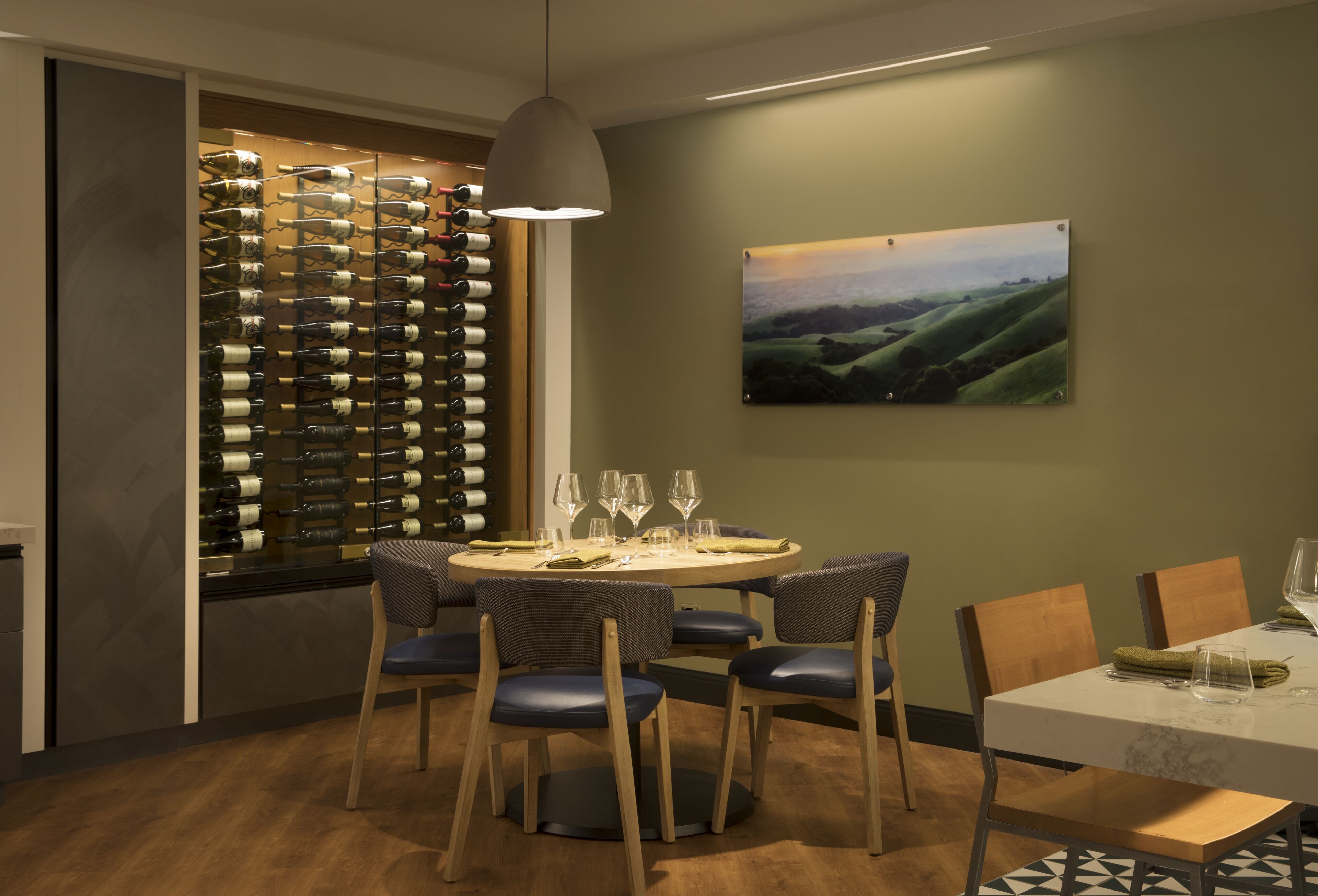 A dining area with a round table, six chairs, and a wine rack with bottles.