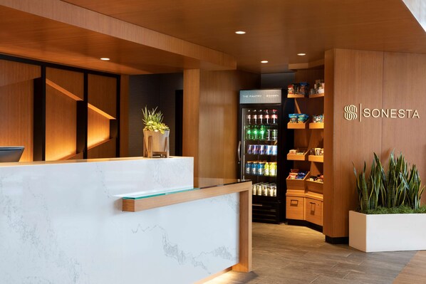 Un área de recepción con mostrador de mármol, estanterías de madera, un refrigerador y una planta en maceta.