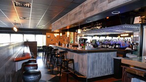 A bar area with stools, a counter, and a variety of bottles and glasses.