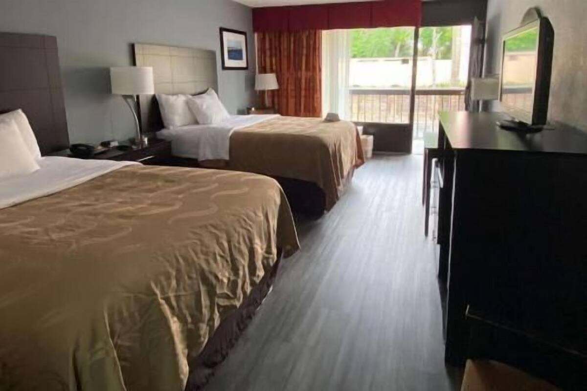 A hotel room with two beds, a desk, a chair, a TV, and a window with a view.