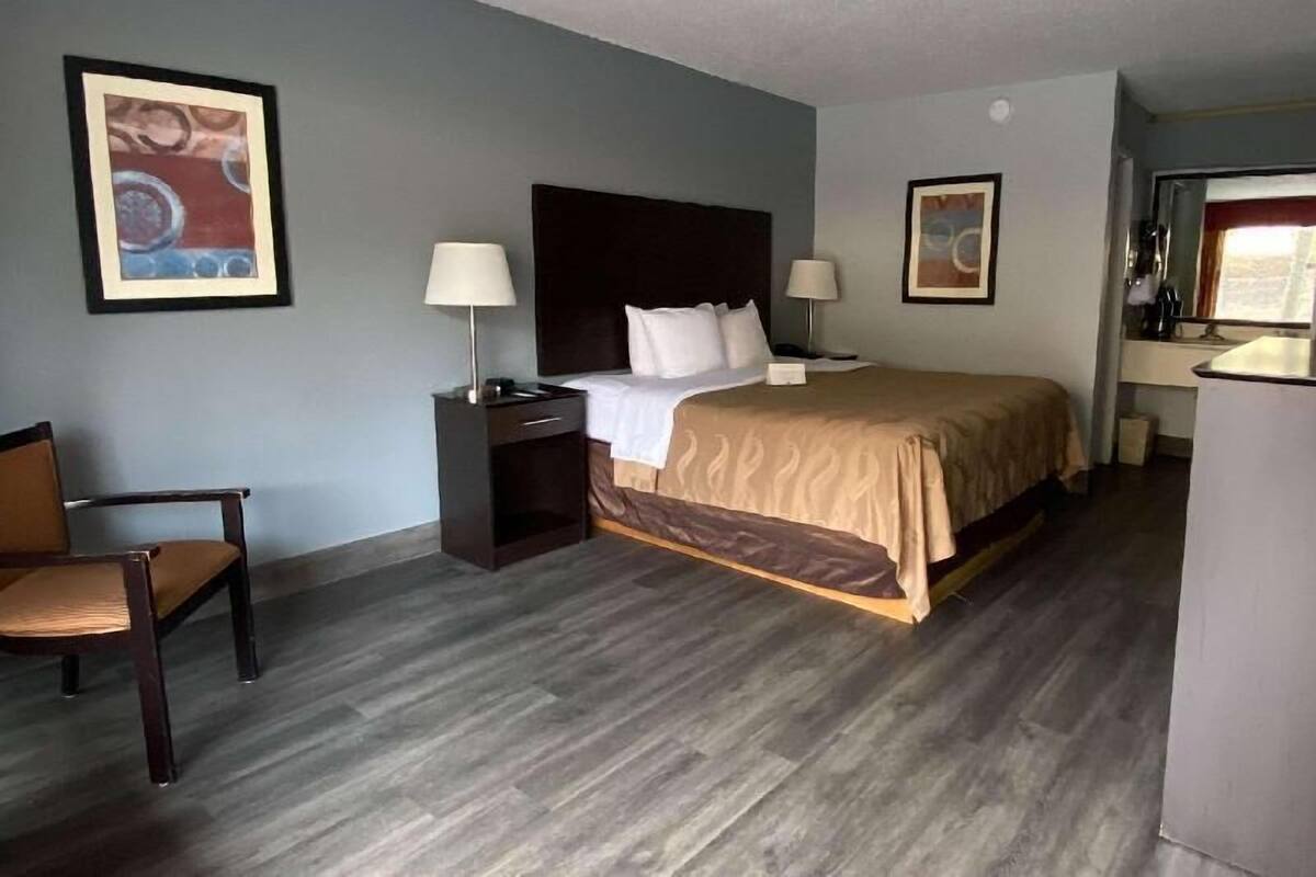 A hotel room with a bed, bedside tables, a chair, and artwork on the walls.