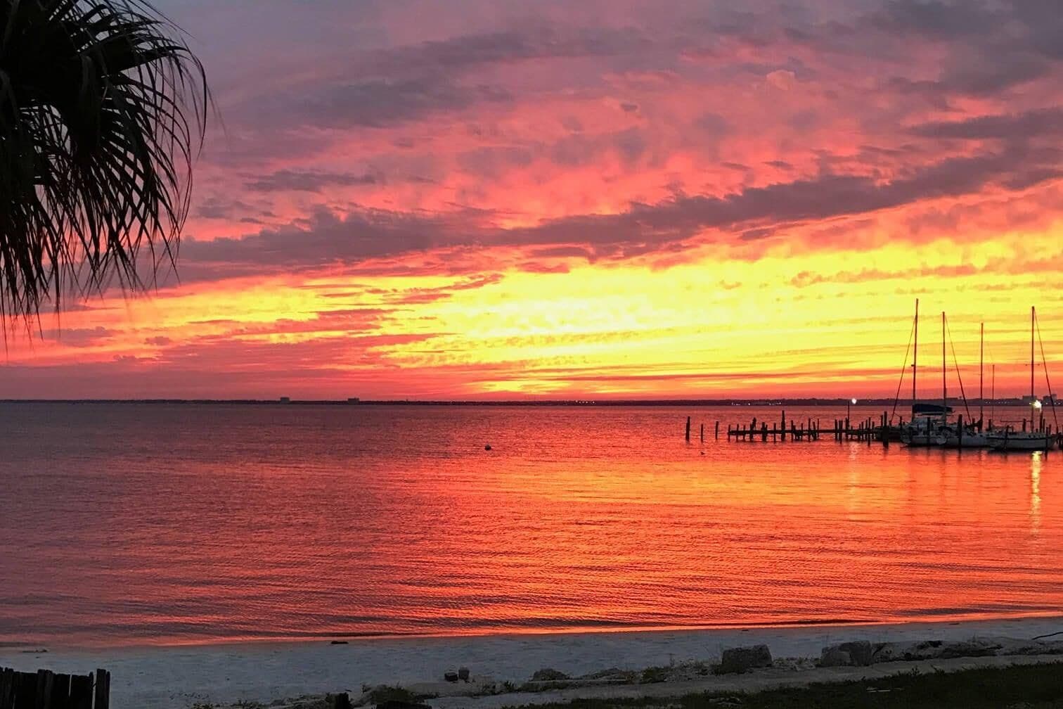 A sunset over a calm sea with a dock and boats.