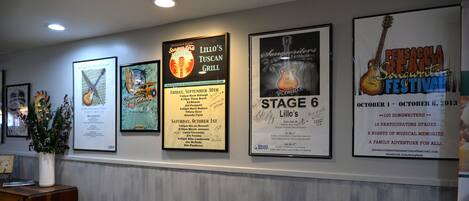 A wall with various framed posters and a wooden desk with a vase.
