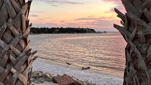 A beach view framed by a woven structure, with calm water and a sunset.