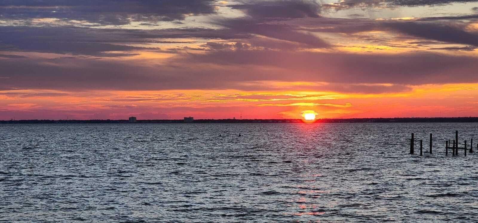 A sunset over a body of water with a distant shoreline and a few buildings.