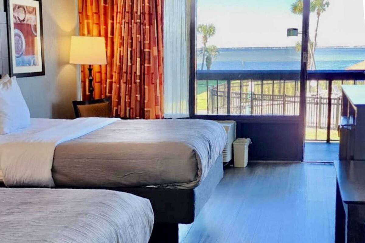 A hotel room with a bed, a nightstand, a lamp, and a view of the ocean.