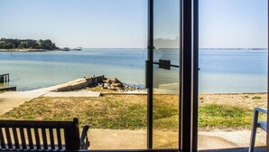 A view from a covered outdoor area with a bench, a glass door, and a view of the sea and distant shoreline.