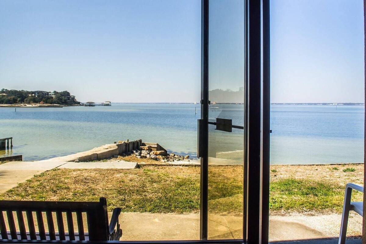 A view from a covered outdoor area with a bench, a glass door, and a view of the sea and distant shoreline.