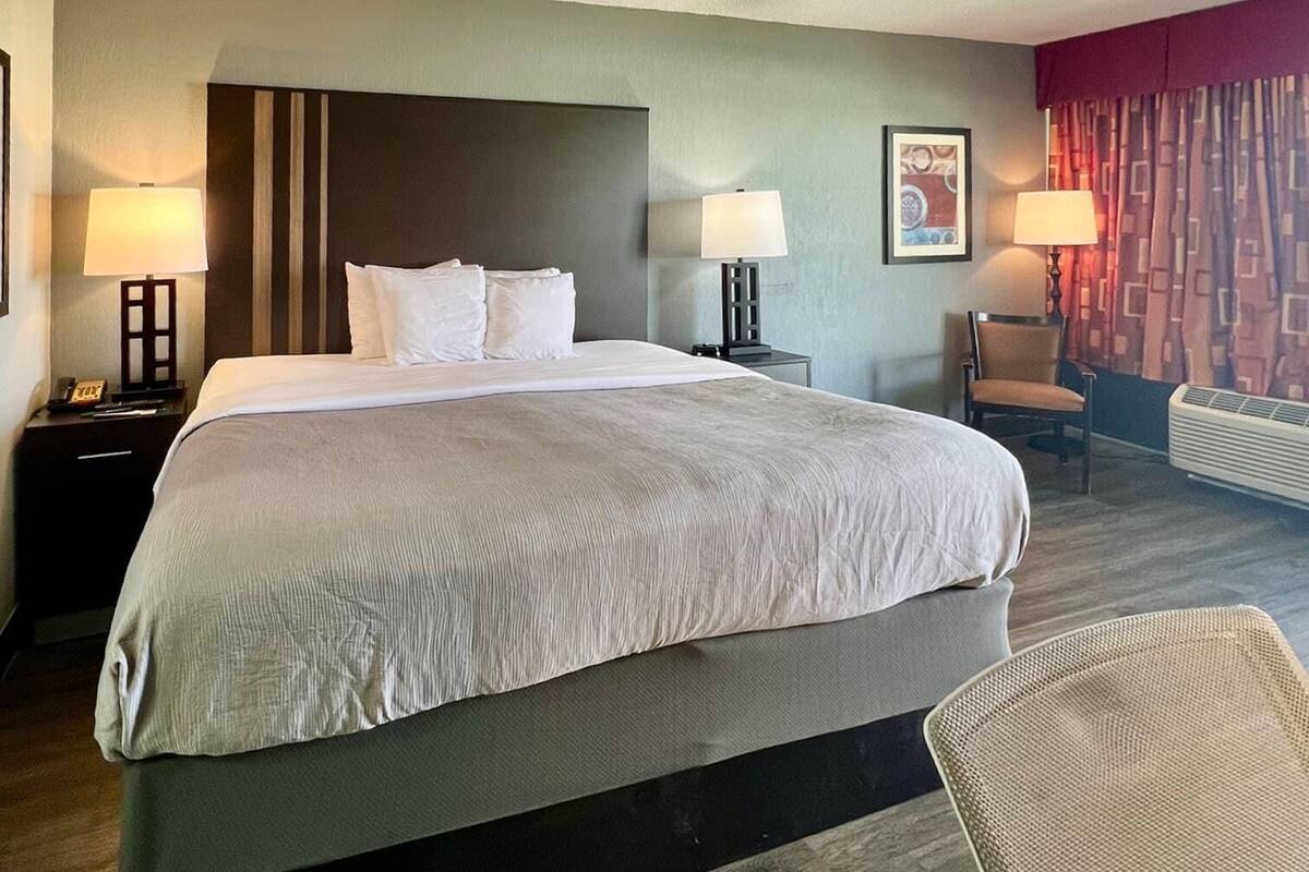 A hotel room with a large bed, two bedside tables with lamps, a chair, and a wall-mounted air conditioner.