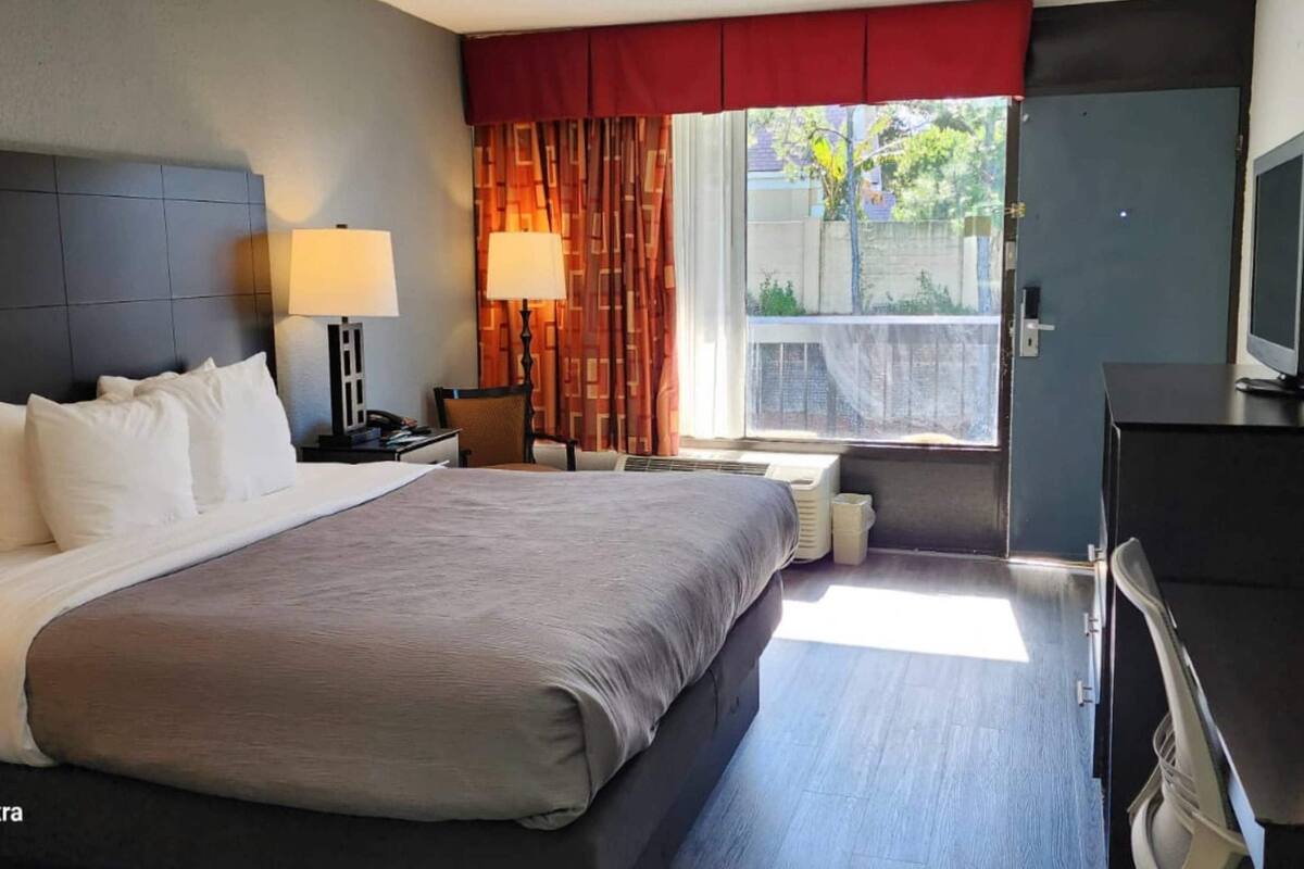 A hotel room with a large bed, two bedside lamps, a TV, a desk, and a window with curtains.