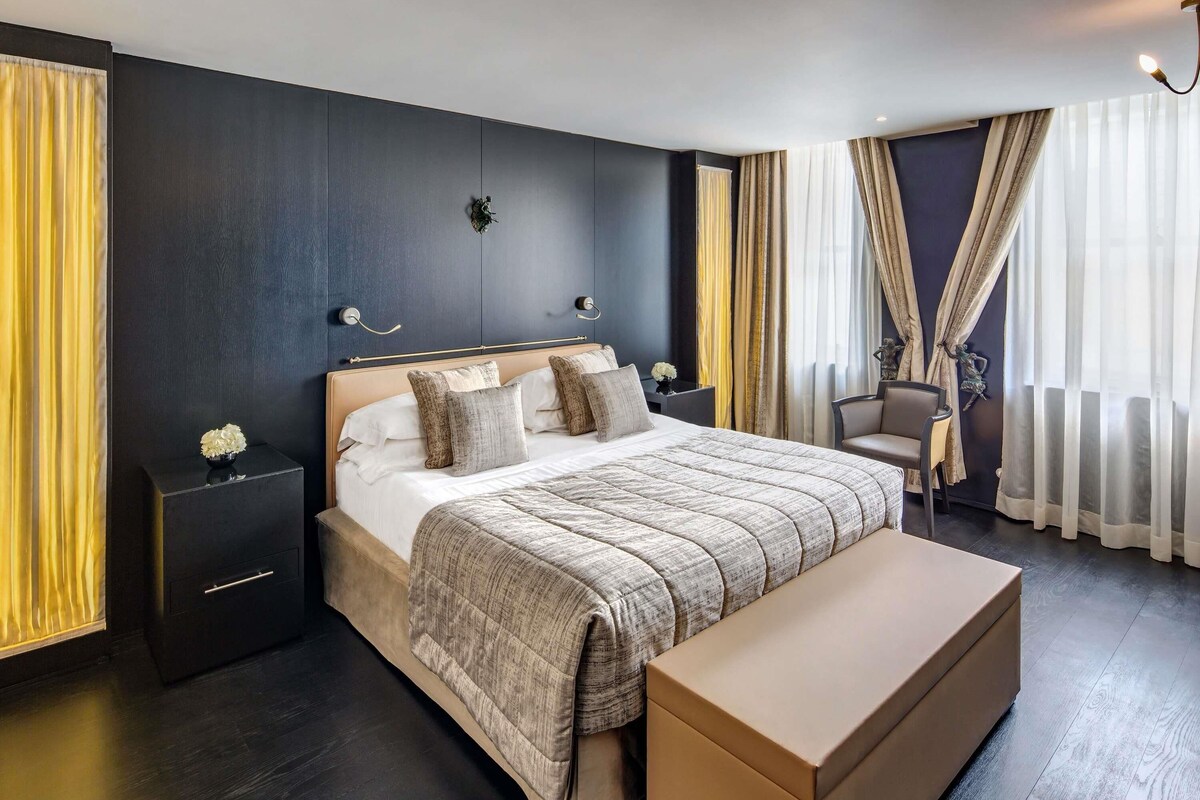 A modern hotel room with a large bed, bedside tables, a bench, and a chair.