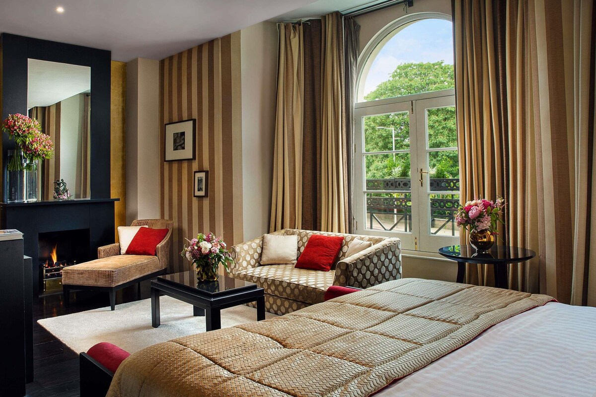 Une chambre d’hôtel avec un grand lit, deux fauteuils, une table basse et une cheminée.