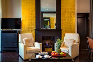 A modern living room with two armchairs, a coffee table with fruit and snacks, a fireplace, and a TV on the left. - Delano London (London)
