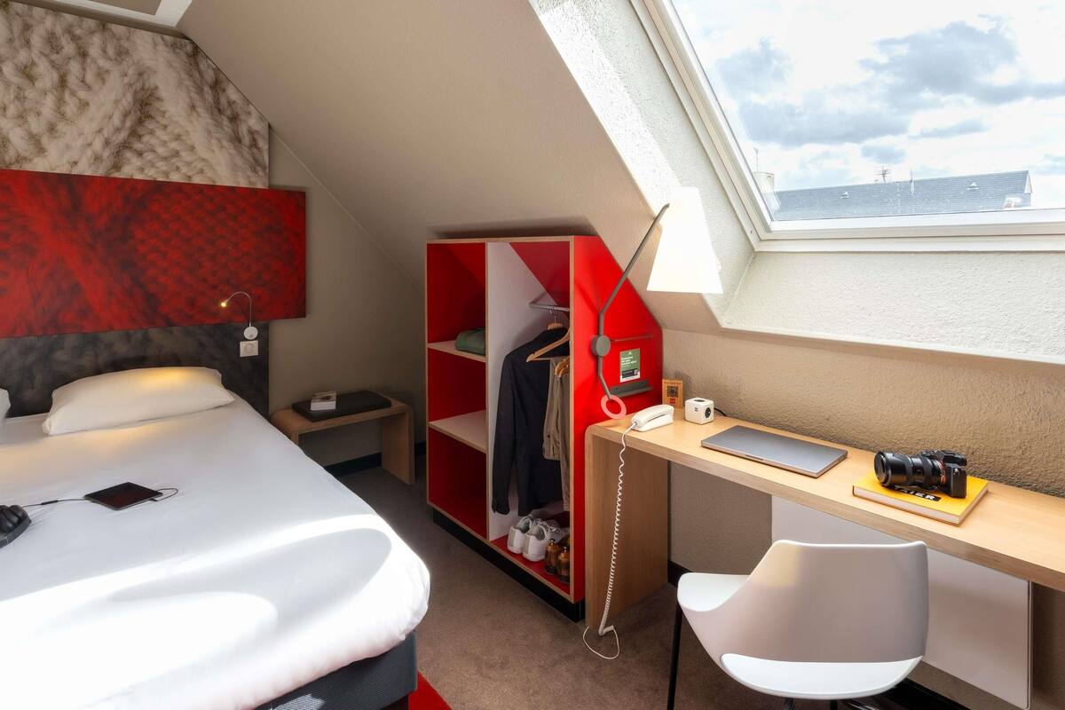 Ein Hotelzimmer mit Bett, Schreibtisch, Stuhl, Kleiderschrank und Dachfenster.