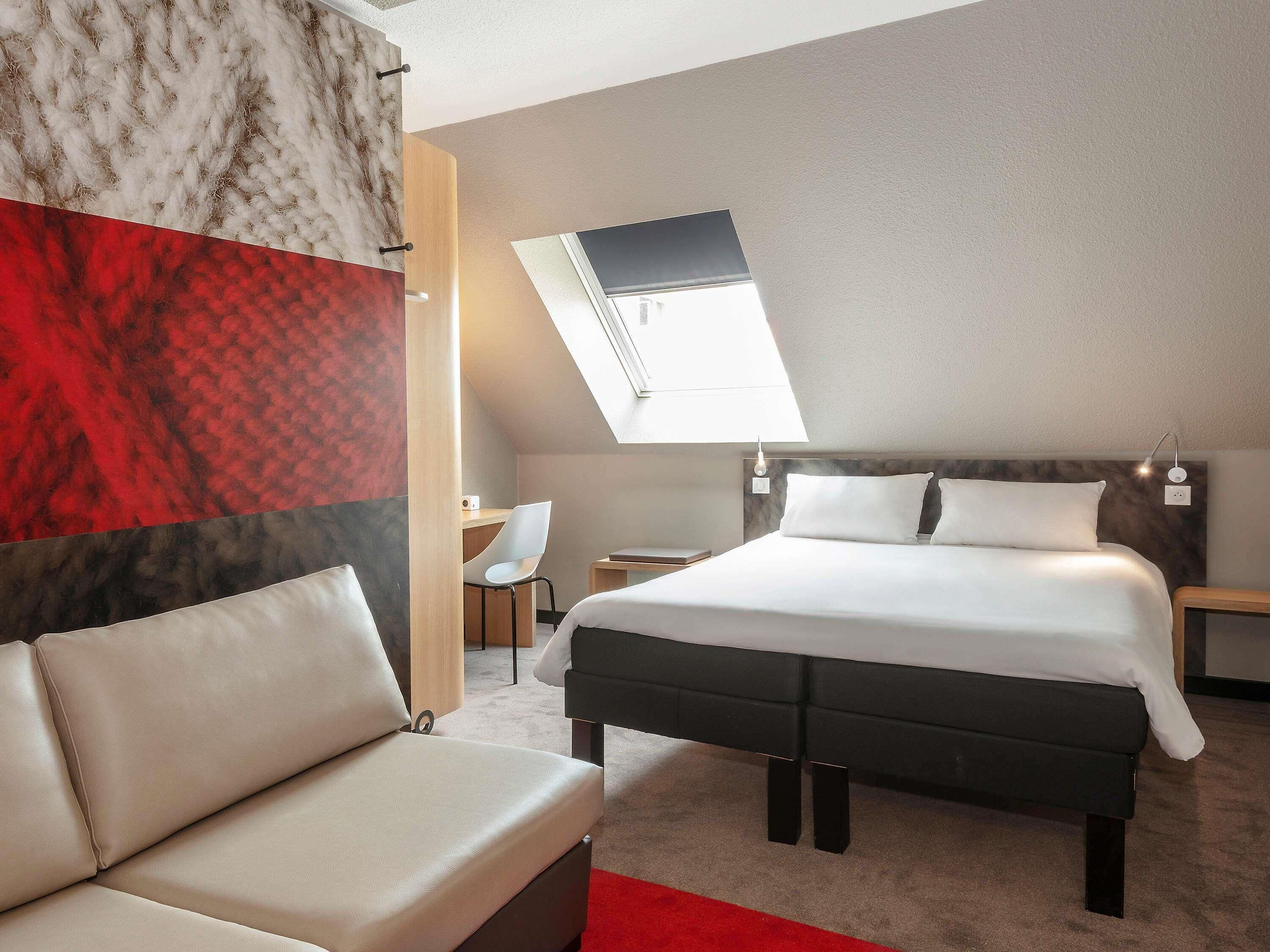 Een moderne hotelkamer met een bed, een bank, een bureau en een dakraam.