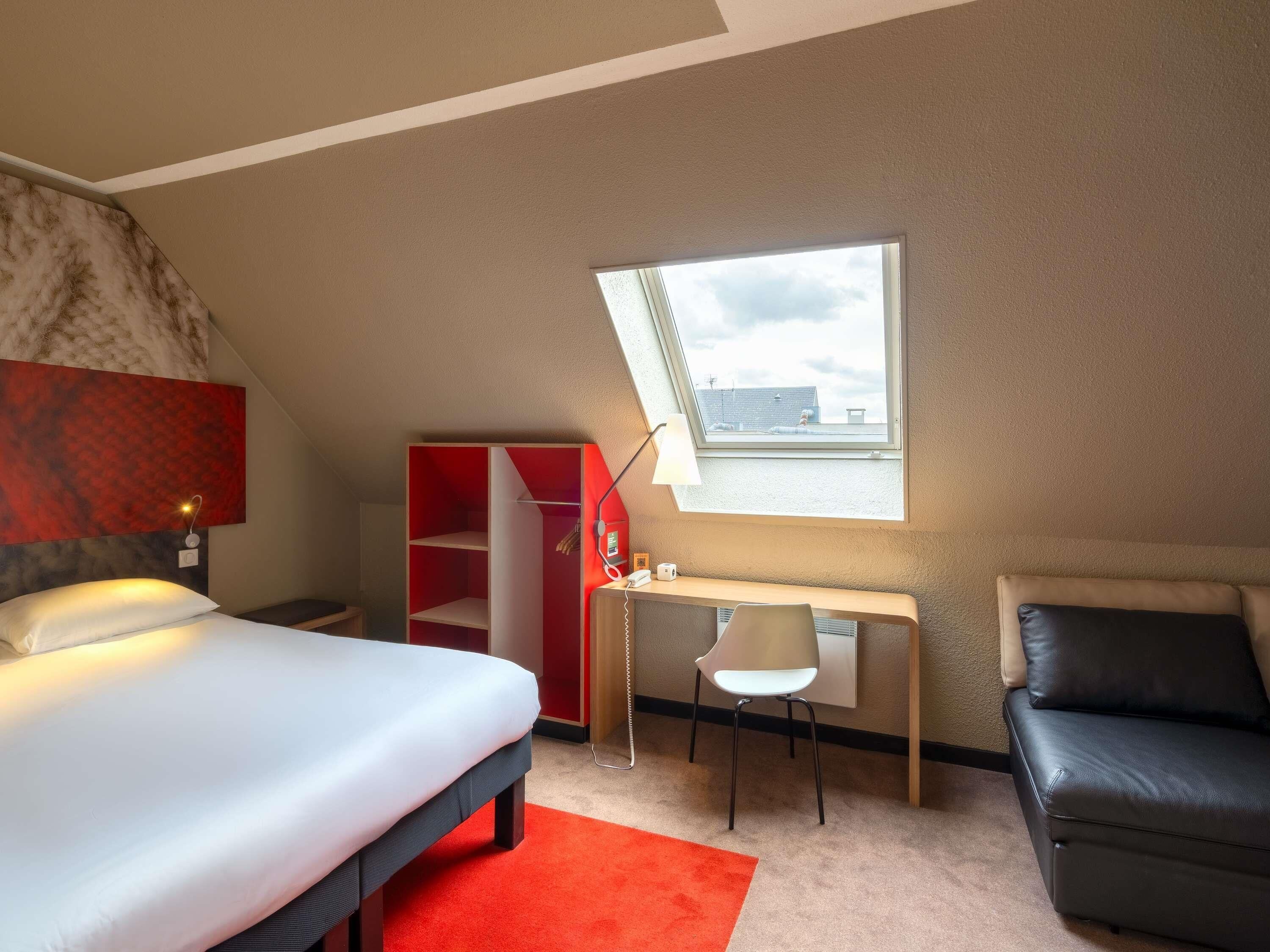 Ein Schlafzimmer mit Bett, Schreibtisch, Stuhl, Kleiderschrank und Dachfenster.