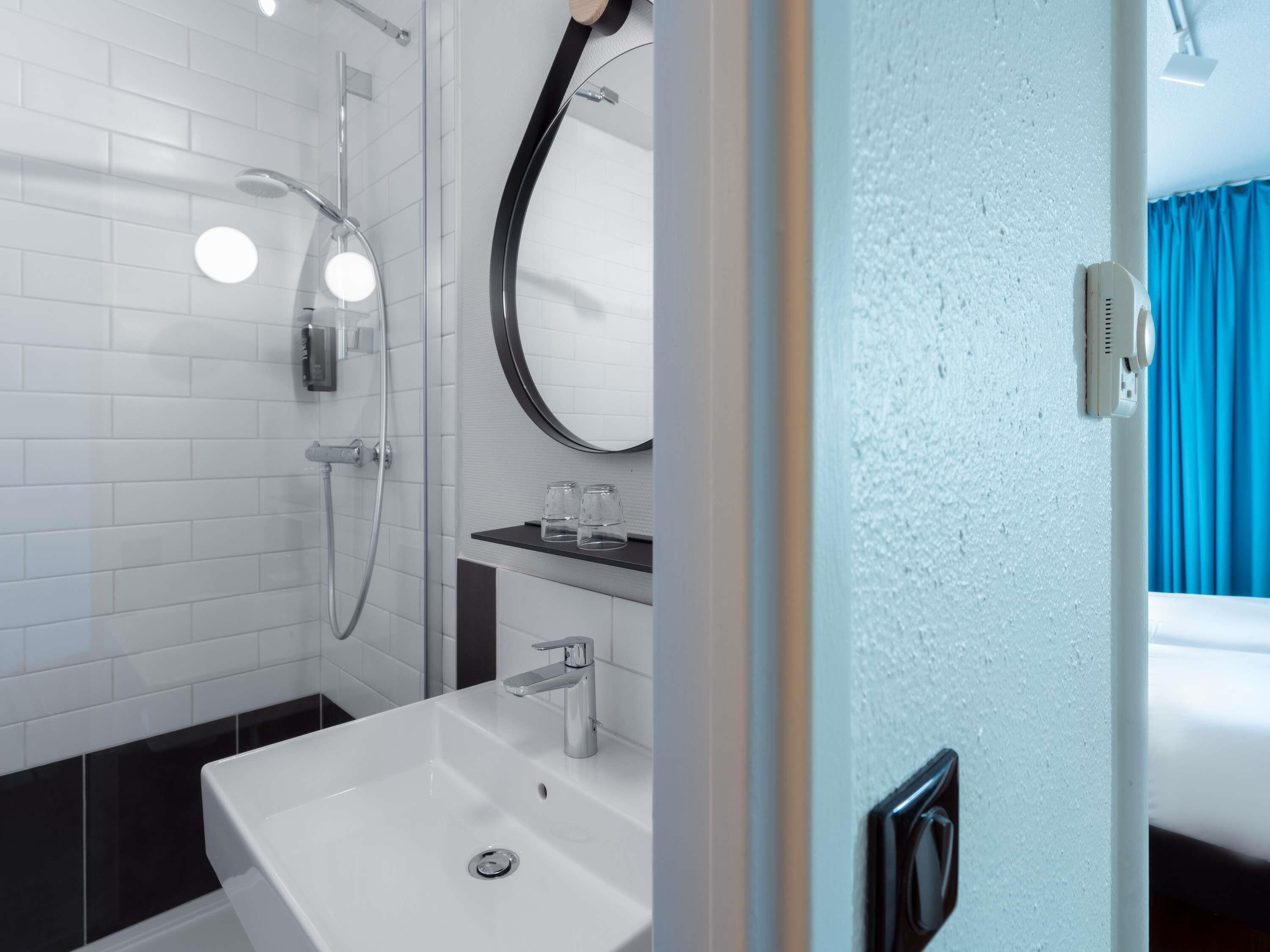 A modern bathroom with a white sink, a glass-enclosed shower, and a round mirror.