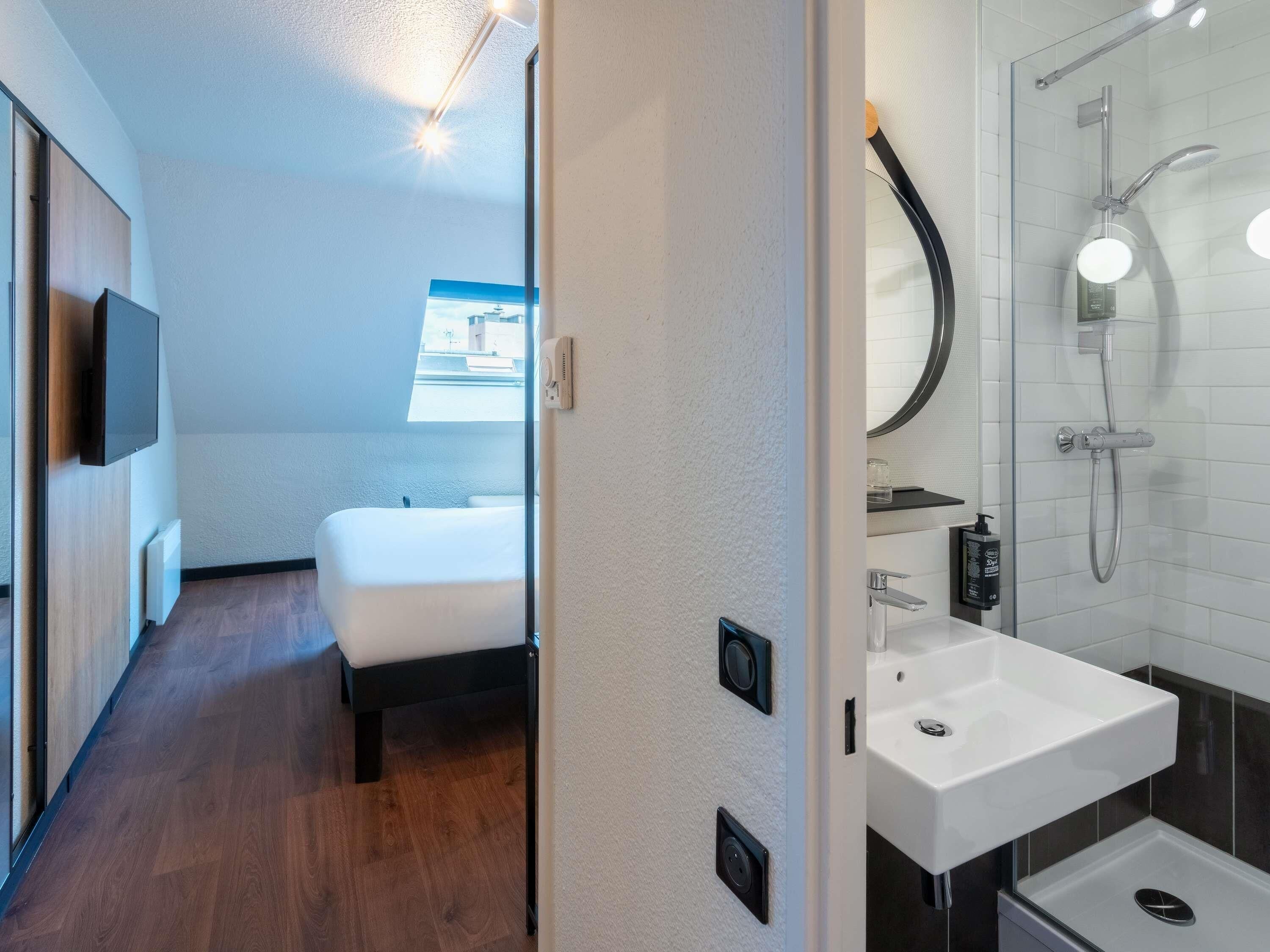 Una habitación de hotel moderna con cama, baño con ducha y vistas a la ciudad.