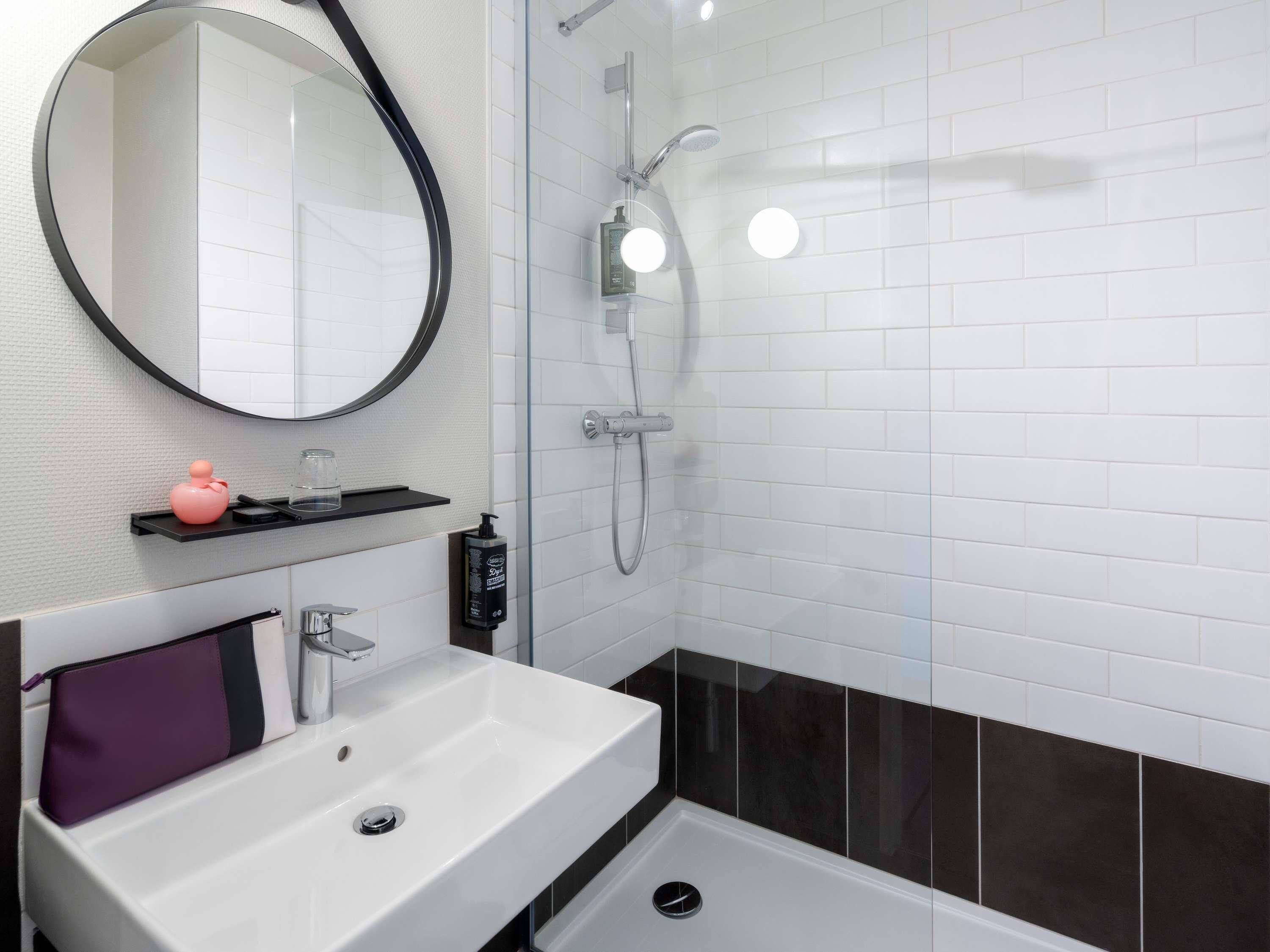 A modern bathroom with a white sink, a mirror, a shower, and a black and white tiled wall.