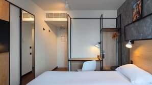 A hotel room with a bed, a desk, a chair, a wardrobe, and a wall-mounted shelf. - ibis Epernay Centre Ville (Epernay)