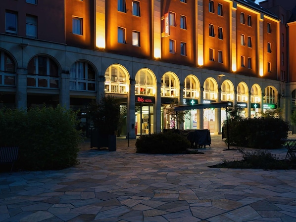 A hotel with arched windows, a stone-paved courtyard, and a sign for the ibis hotel.
