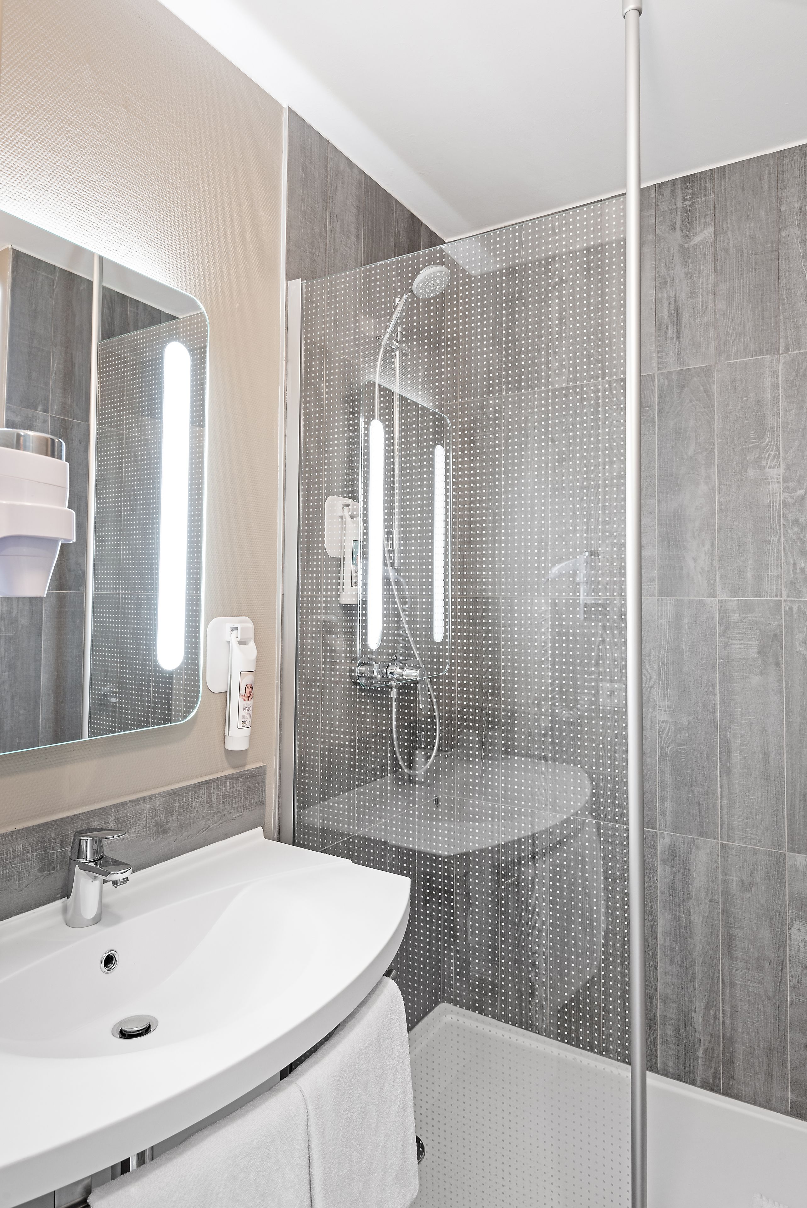 Un bagno moderno con un lavandino curvo, uno specchio grande, una cabina doccia in vetro e un asciugamano appeso al muro.