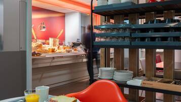 Een ontbijtbuffet met diverse soorten eten, een persoon op de achtergrond en een feloranje stoel.