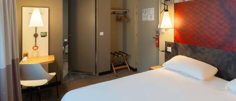 Een hotelkamer met een bed, een bureau met stoel, een lamp, een airconditioning en een deur.