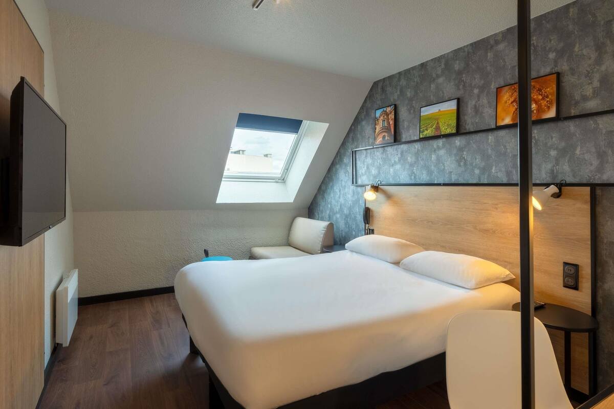 Ein modernes Schlafzimmer mit einem großen Bett, einem Oberlicht, einem an der Wand montierten Fernseher und einem Nachttisch.