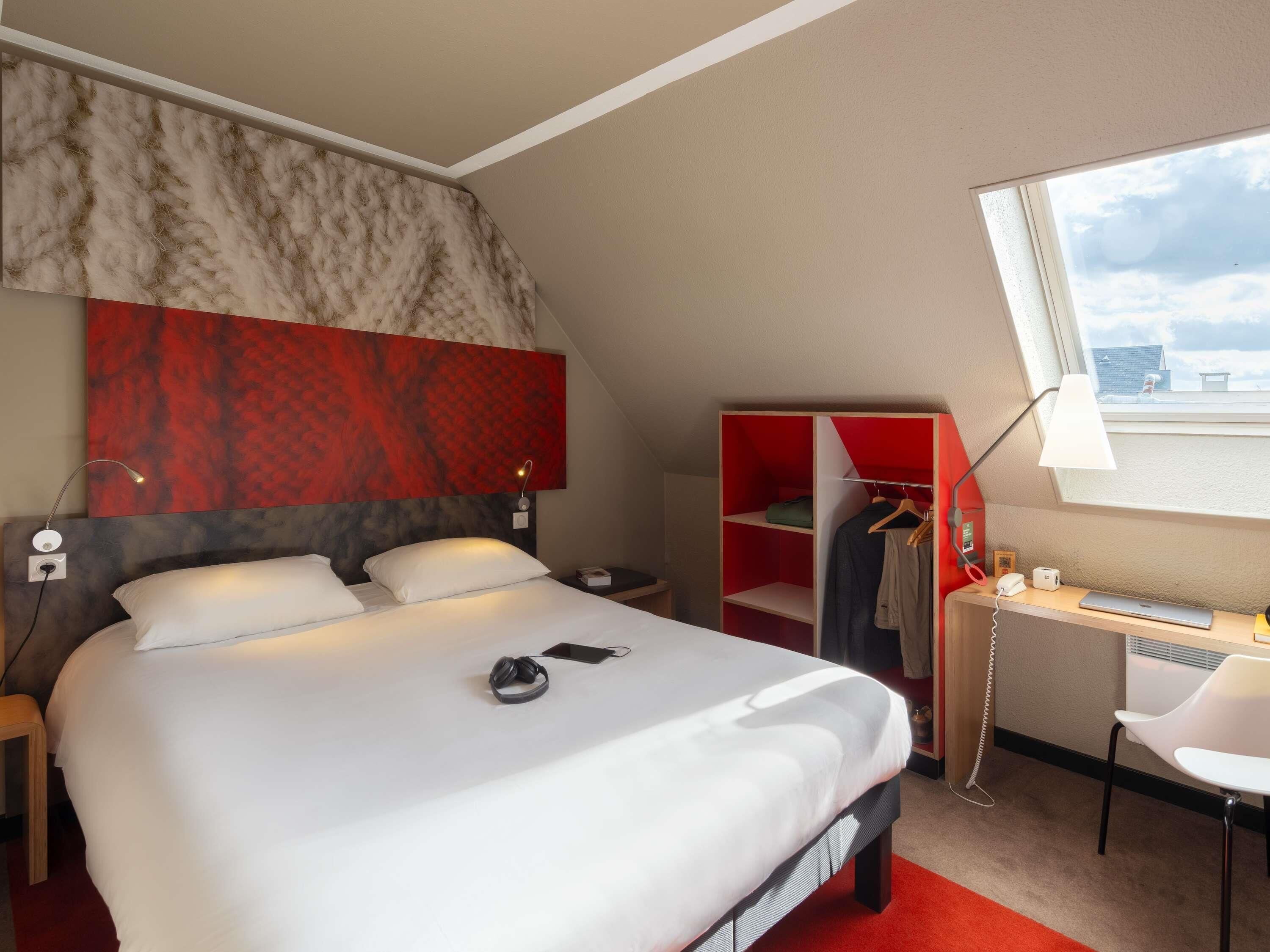 A hotel room with a bed, a desk with a chair, a wardrobe, and a window with a view.