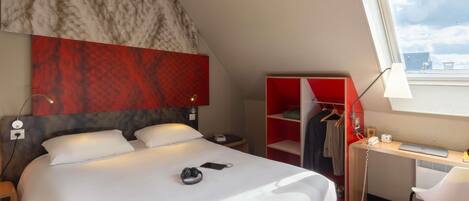 A hotel room with a bed, a desk with a chair, a wardrobe, and a window with a view.
