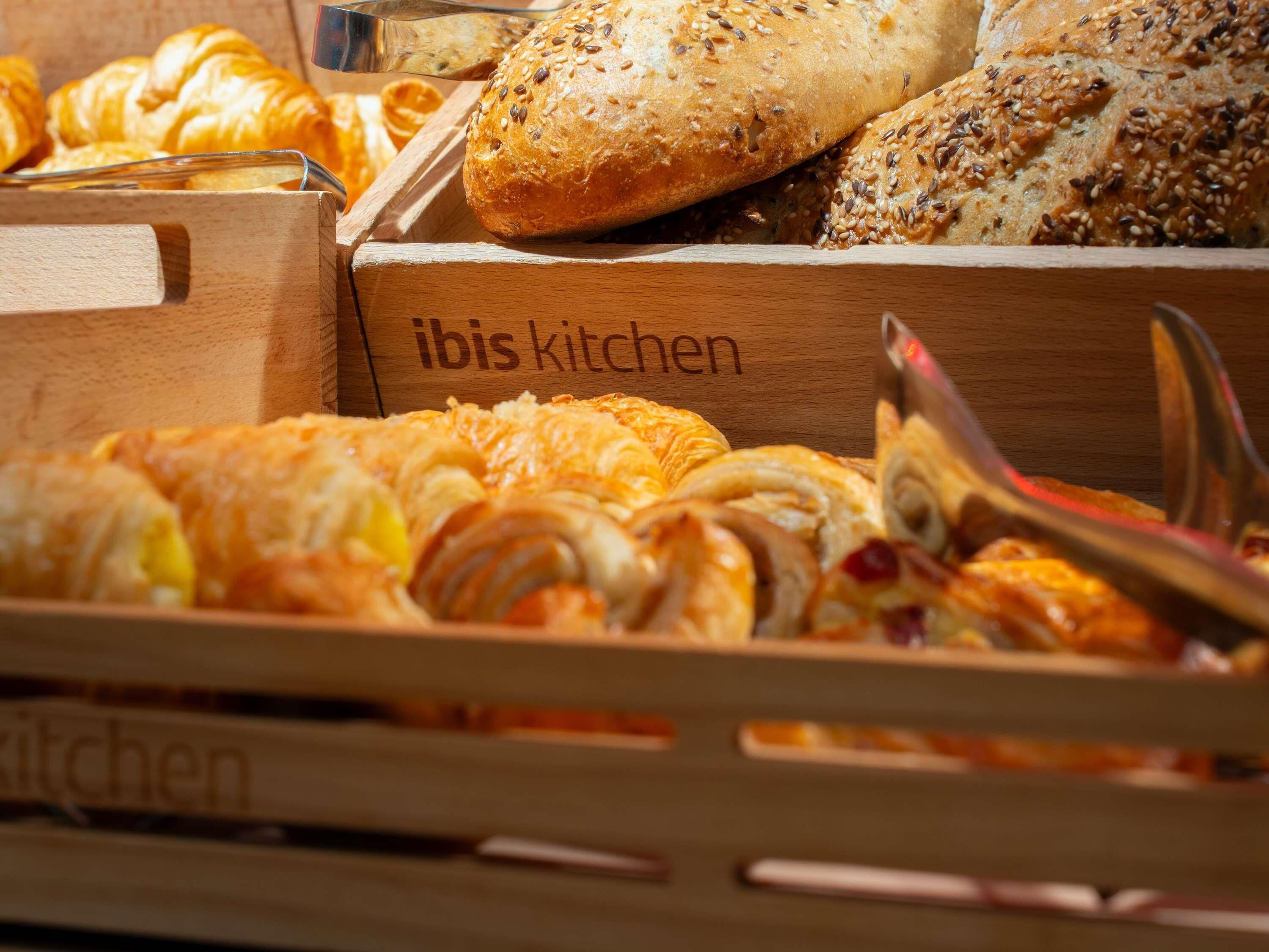 Une variété de produits de boulangerie disposés dans une caisse en bois étiquetée « Cuisine Ibis ».