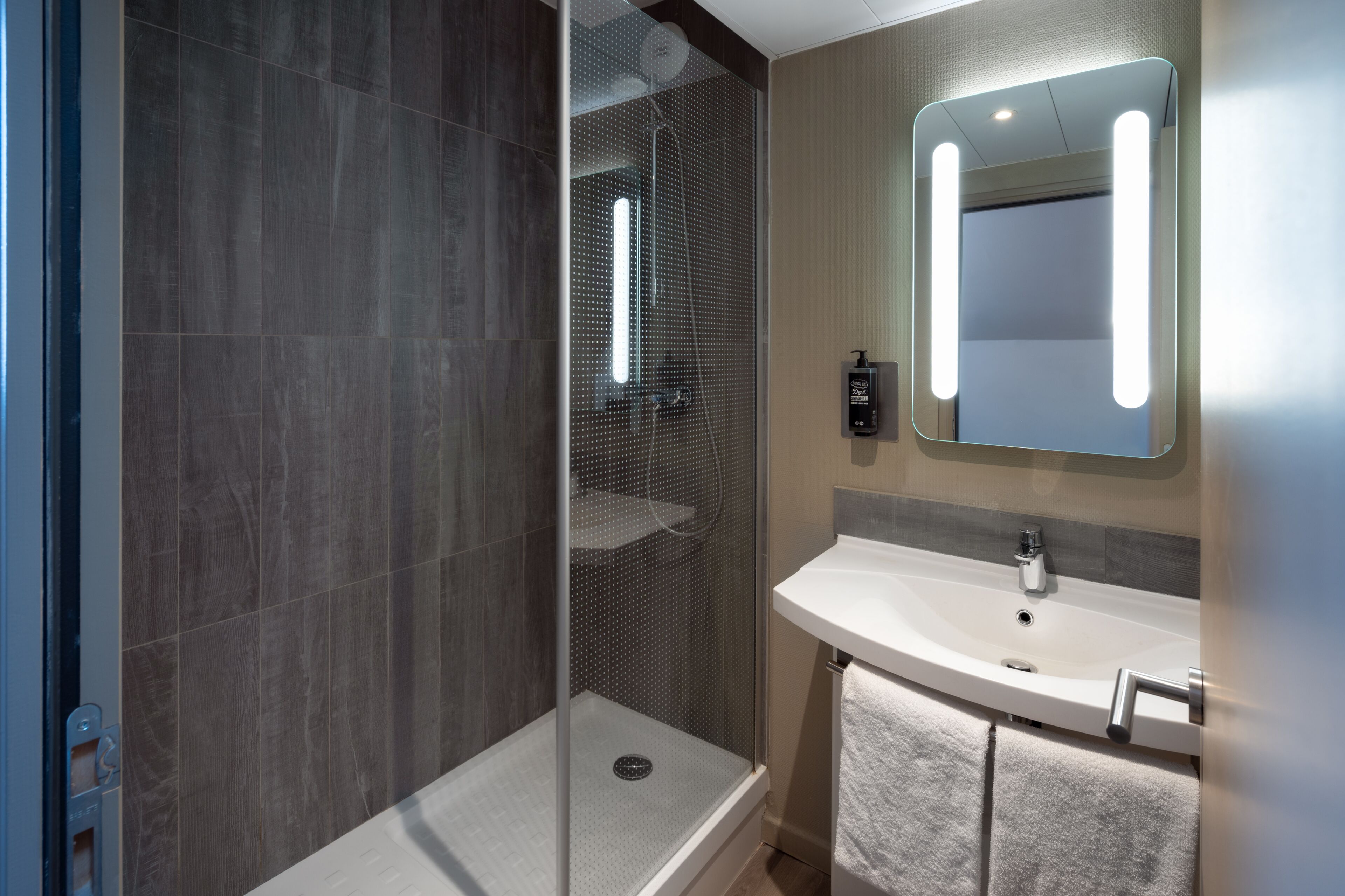 A modern bathroom with a glass-enclosed shower, a white sink, and a mirror with built-in lighting.