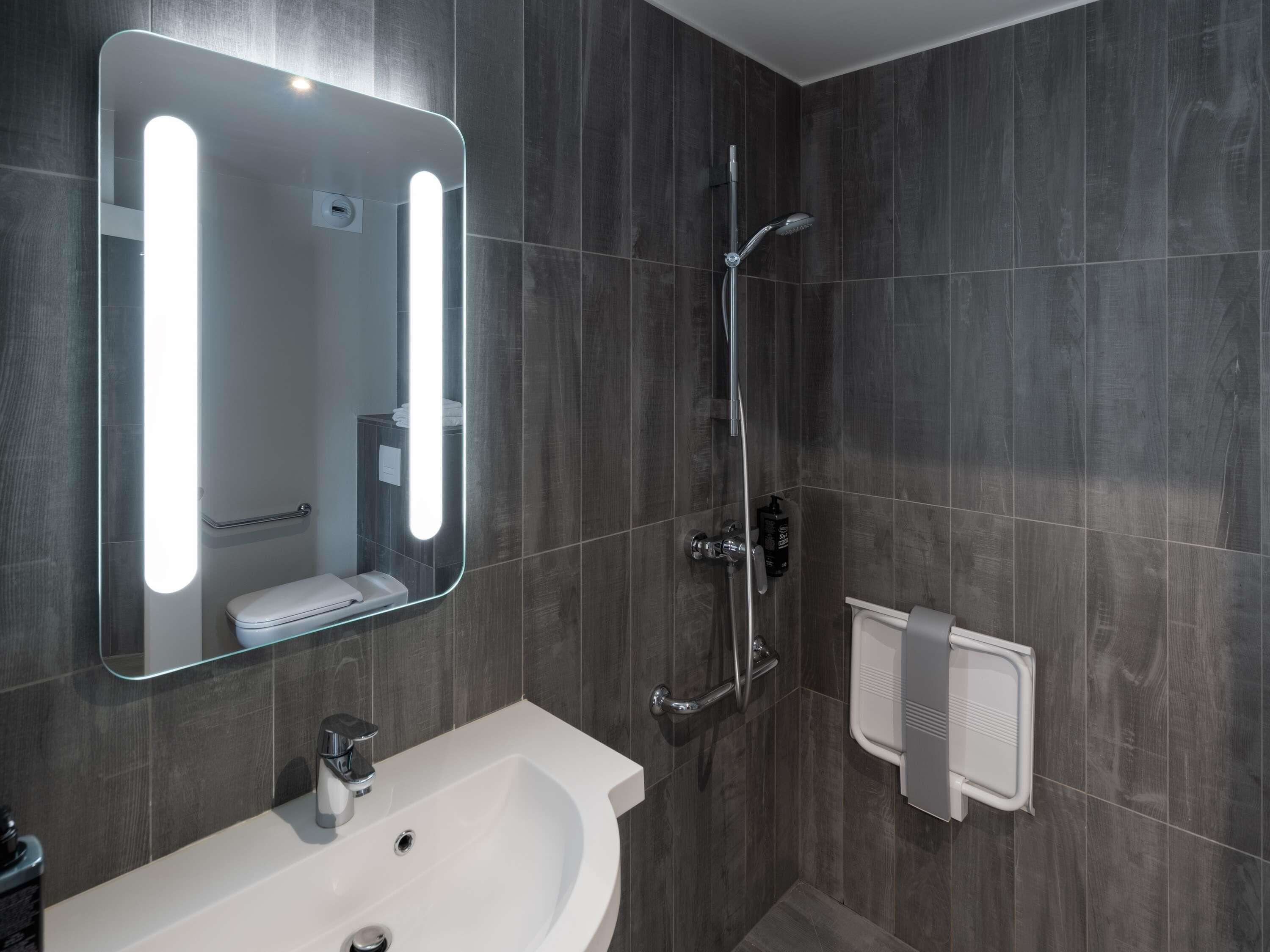 A modern bathroom with a large mirror, a sink, a shower, and a towel rack.