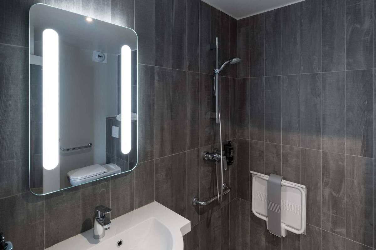 Ein modernes Badezimmer mit großem Spiegel, Waschbecken, Dusche und Handtuchhalter.