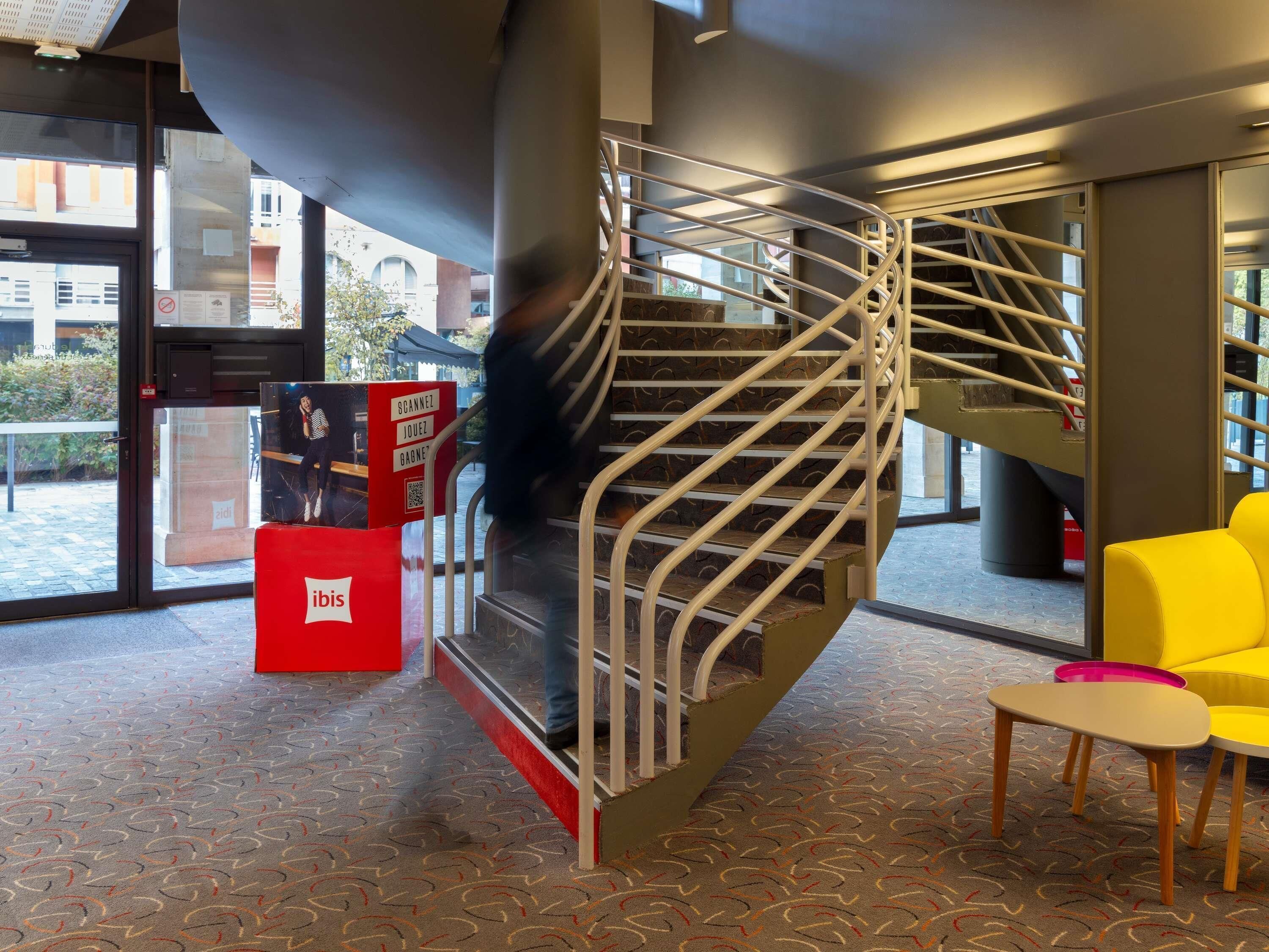 A spiral staircase with metal railings, a red kiosk, and a yellow chair in a modern interior space.