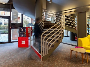 A spiral staircase with metal railings, a red kiosk with a QR code, and a yellow chair. - ibis Epernay Centre Ville (Epernay)