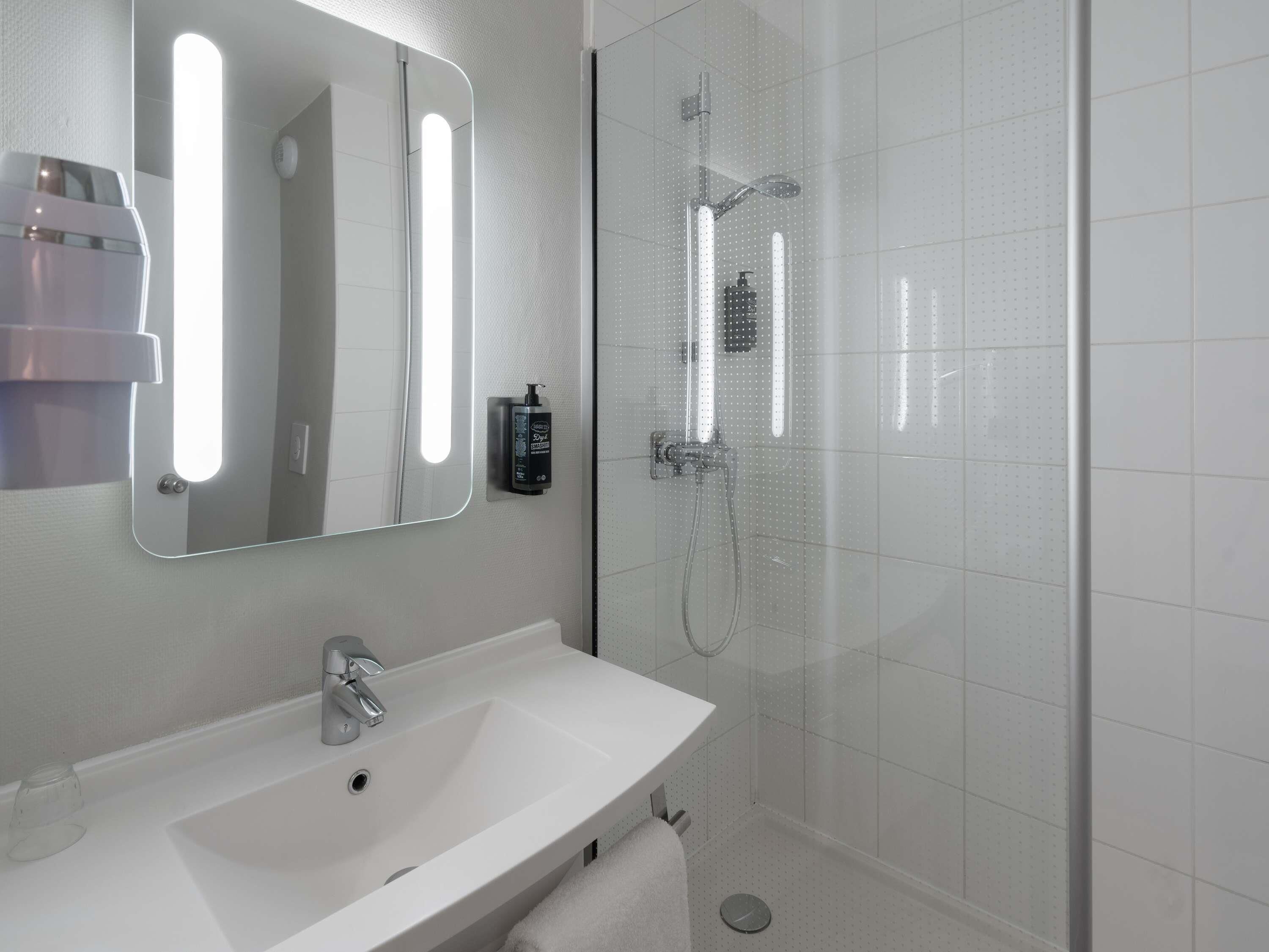 A modern bathroom with a white sink, a mirror, and a glass-enclosed shower.
