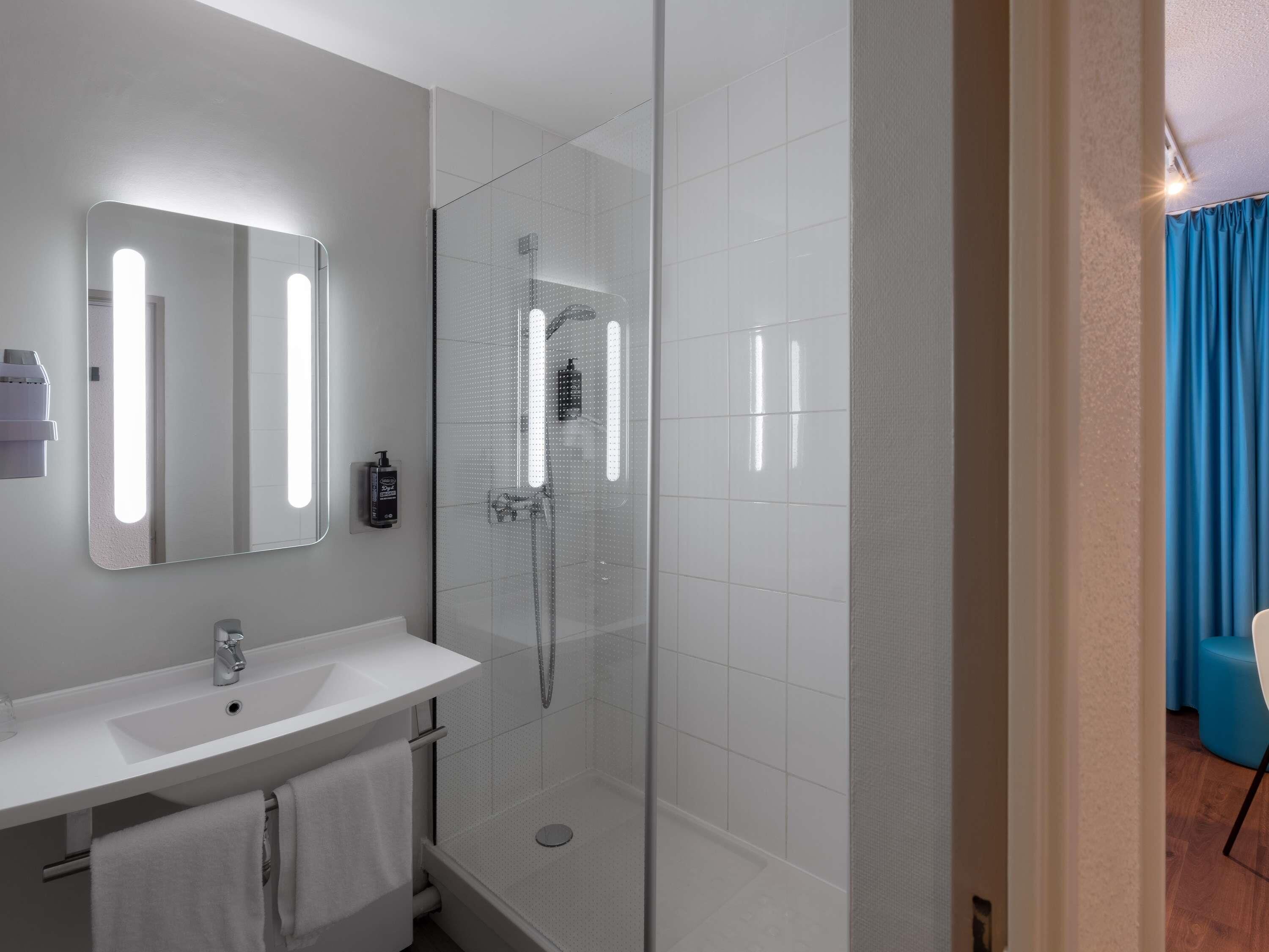 Un baño moderno con ducha envuelta en cristal, un lavabo blanco y un espejo con iluminación integrada.