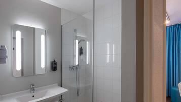 Un baño moderno con ducha envuelta en cristal, un lavabo blanco y un espejo con iluminación integrada.