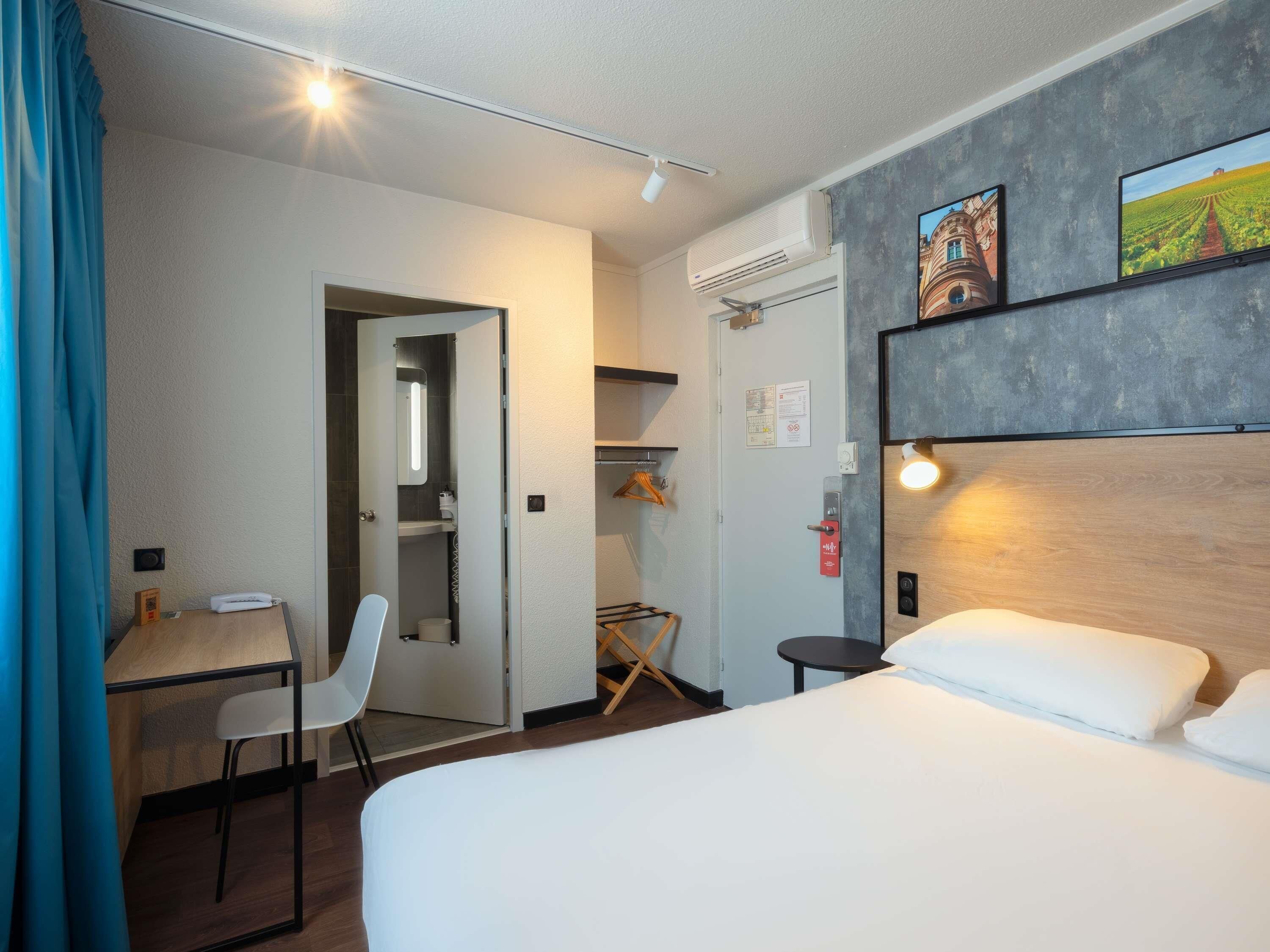 Une chambre d’hôtel comprenant un lit, un bureau, une chaise, une armoire et une douche.