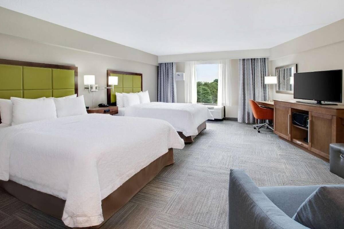 A hotel room with two beds, a desk with a TV, and a view of the outdoors.