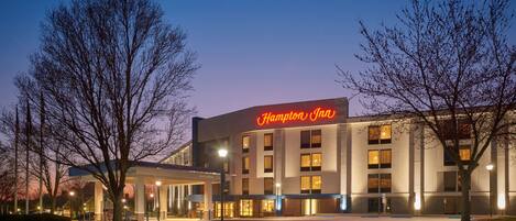 A Hampton Inn hotel with a modern facade, large windows, and a prominent neon sign.