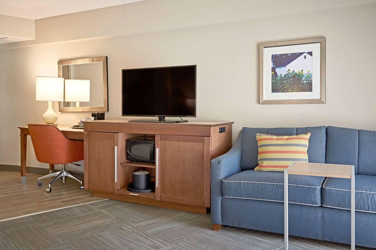A hotel room with a desk, chair, television, sofa, and a framed picture on the wall.