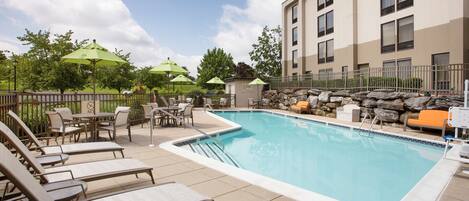 A pool area with lounge chairs, umbrellas, and a stone wall.