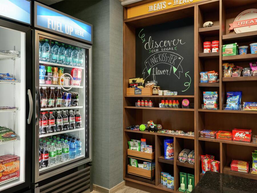 Un refrigerador de bebidas repleto de diversas opciones, junto a una estantería con diferentes aperitivos.