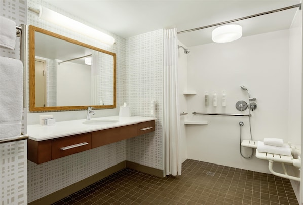 A modern bathroom with a white sink, wooden vanity, a large mirror, a shower with a glass door, and a towel rack.